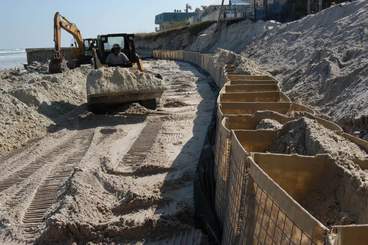 Image: A worker uses a mini front-end loader to place sand into these bags which will act as a temporary seawall