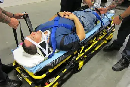 A man on an EMT backboard stretcher getting secured.