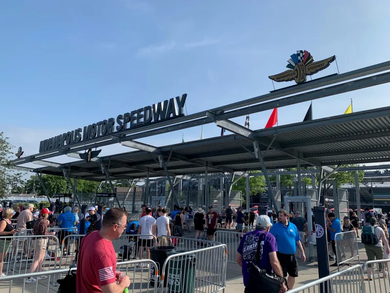 A public entrance to the Indy 500 raceway, showing attendees entering through multiple gates. Above the entrance it reads “Indianapolis Motor Speedway.”