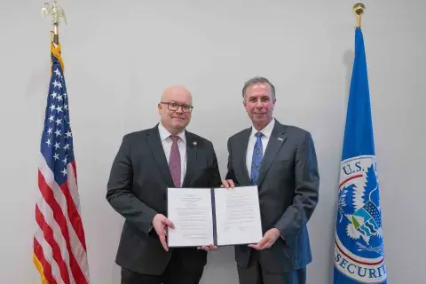 Ambassador Hautala and Under Secretary Kusnezov pictured holding the signed Joint Statement of Intent standing next to the United States and DHS flags. 