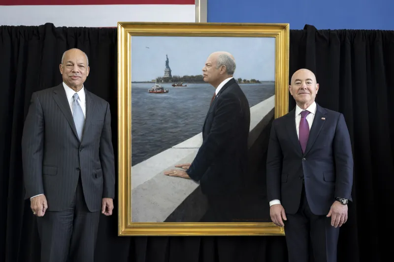 Secretary Mayorkas and former Secretary Johnson pose next to former Secretary Johnson's portrait