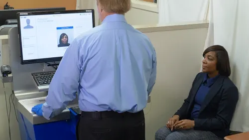 An applicant sits near a USCIS employee using a computer that is processing her photo