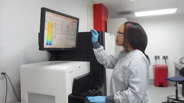 A molecular biologist at the NBACC forensic laboratory examines a DNA sample in front of the Illumina HiSeq high capacity DNA sequencing instrument. 