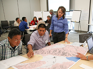 A photograph of a group of tribal representatives gathered around a table reviewing maps.